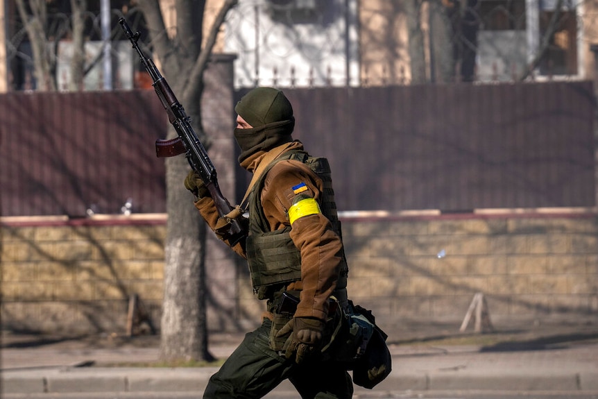 A Ukrainian soldier runs holding his weapon outside a military facility, in Kyiv.
