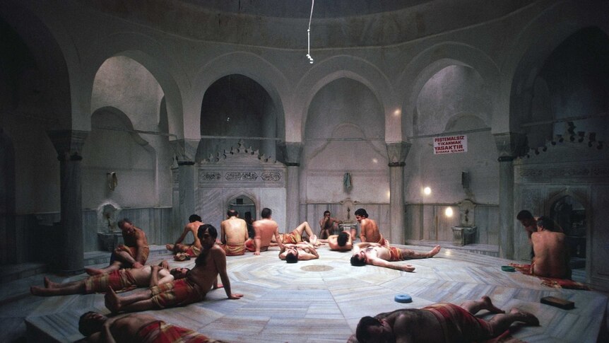A large circular ornate room with a central platform where a group of men are relaxing.