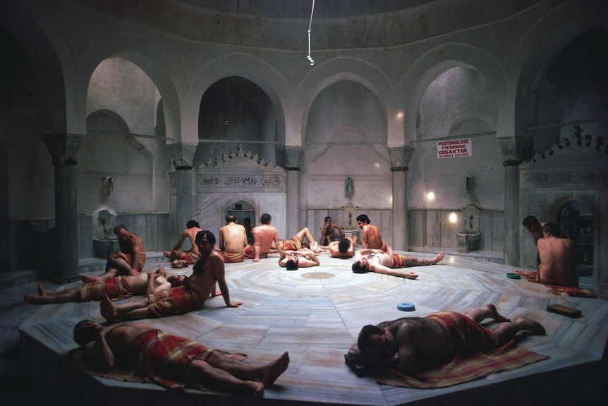 A large circular ornate room with a central platform where a group of men are relaxing.