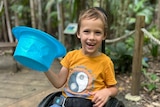 zach in his wheechair smiling, lifting a blue plastic top hat