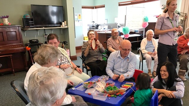 A group of elderly aged care residents interact with a young child.