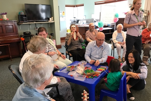 A group of elderly aged care residents interact with a young child.
