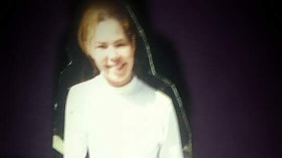 A blurry picture of a smiling teenage girl wearing a white turtleneck.