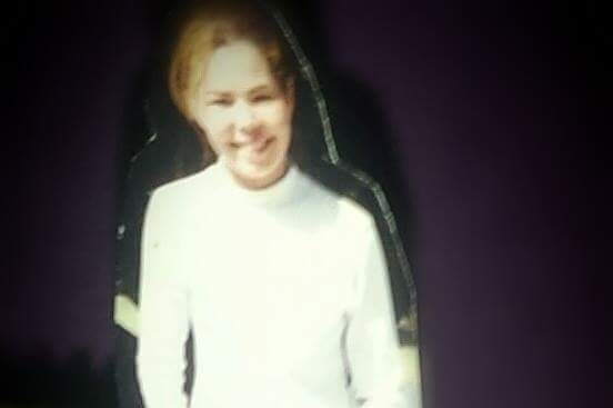 A blurry picture of a smiling teenage girl wearing a white turtleneck.