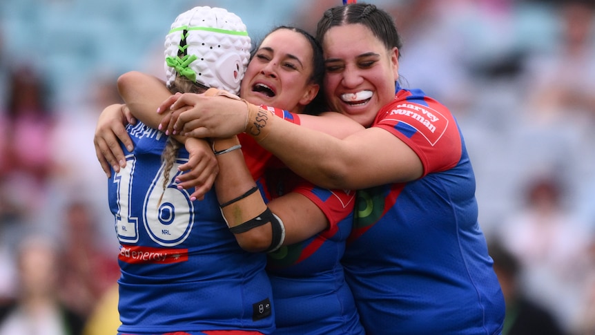 Three NRLW players embrace in a hug, one crying, after winning the premiership