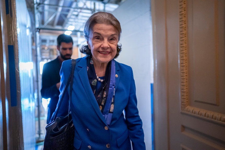 Dianne Feinstein in a blue suit walking down the halls of the Senate.