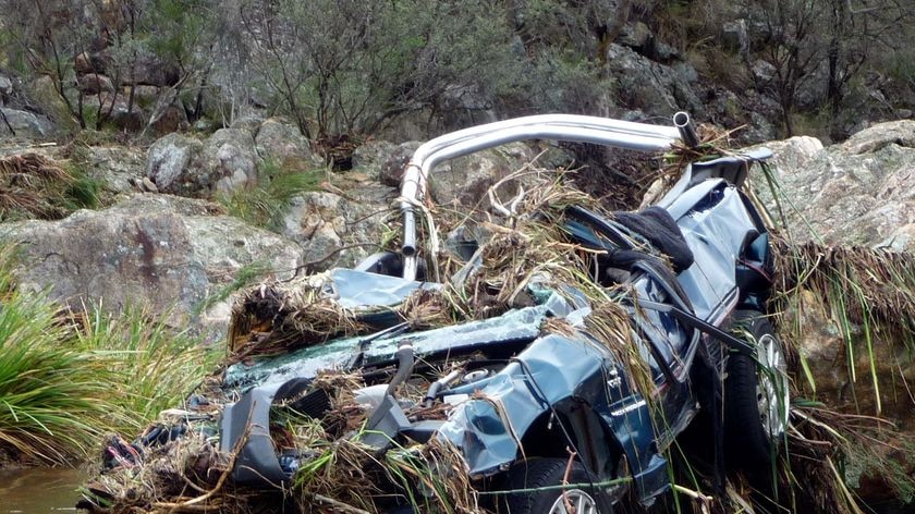 A car lies in a severely damaged state in a flooded creek