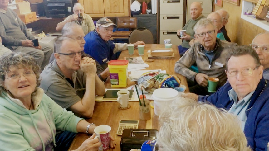 Group of men and women sitting around a table smiling and having a cuppa.