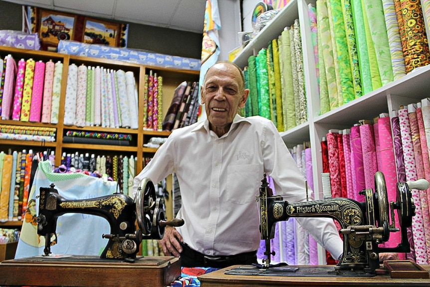 Sewing machine repairman Peter Taylor stands with two vintage sewing machines.