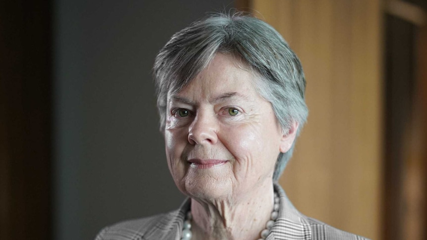 A woman with grey hair wearing a check jacket and pearls