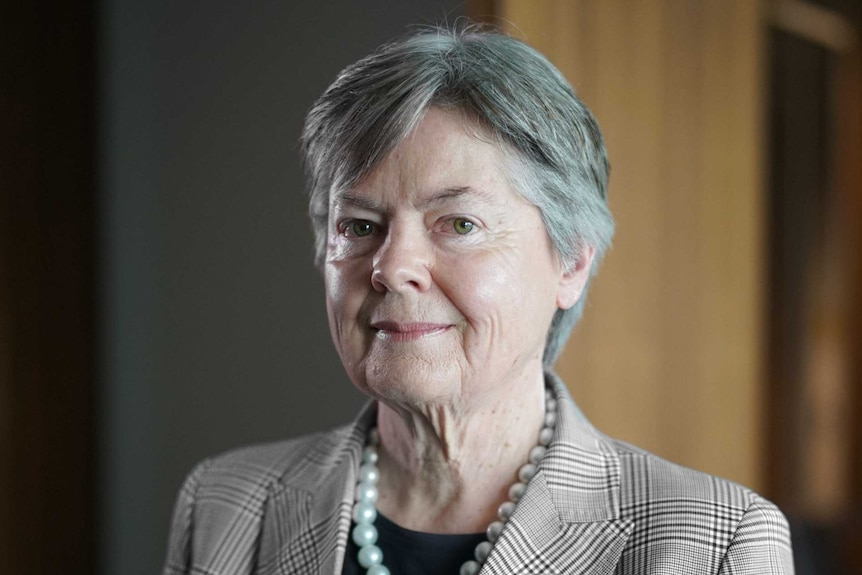 A woman with grey hair wearing a check jacket and pearls