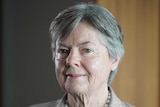 A woman with grey hair wearing a check jacket and pearls