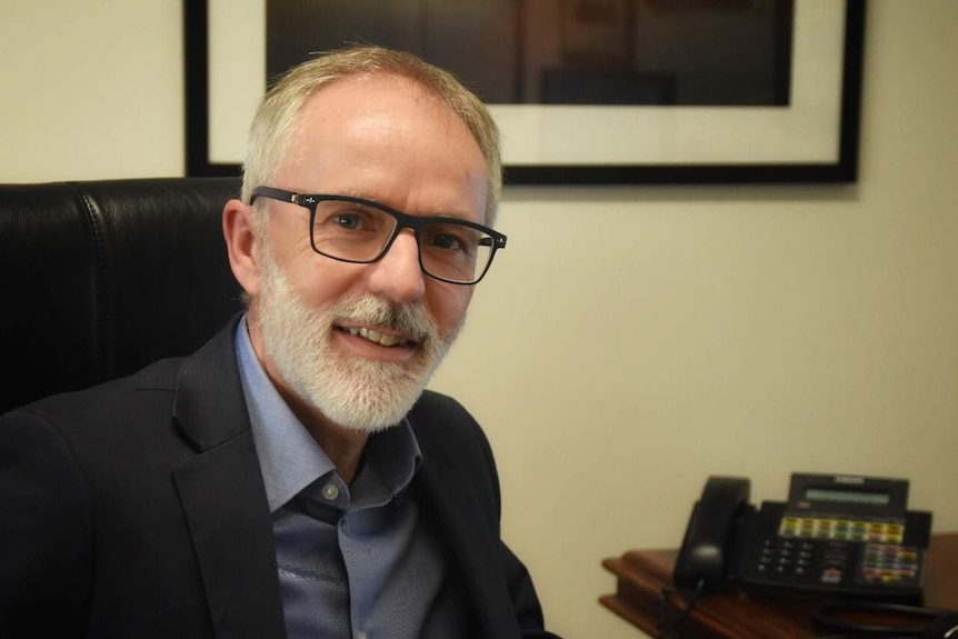 Dr David Wilson sits at a desk and smiles for the camera.