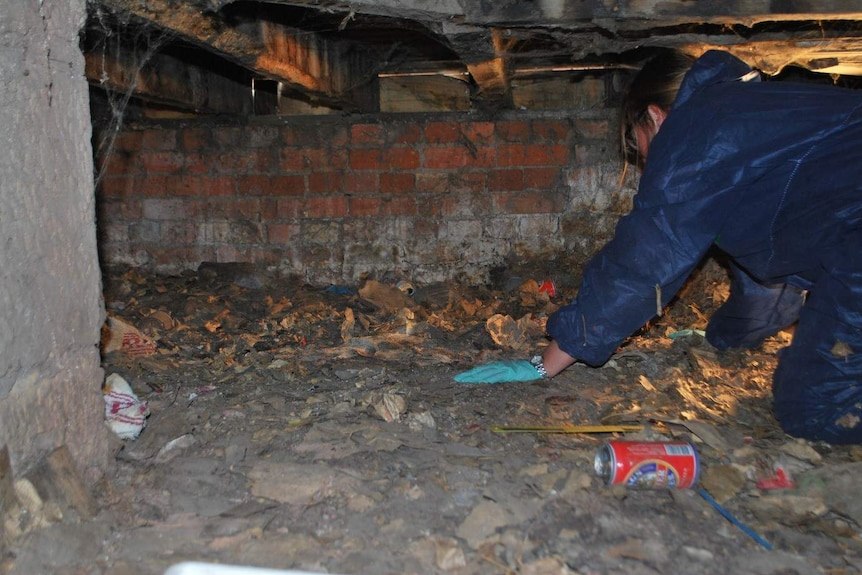 A woman in a blue hazard suit climbs through a small, enclosed space