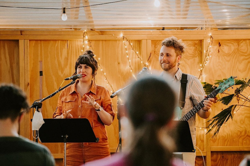 a man and a woman stand on stage, she is singing and he plays guitar.