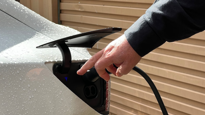 A man's hand charging a while electic car. 