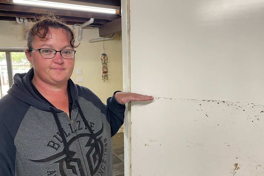 Woman indicates flood marking on wall up to her chest