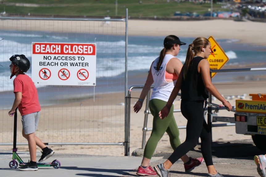 Two women and a child walk next to a Beach Closed sign in Bondi