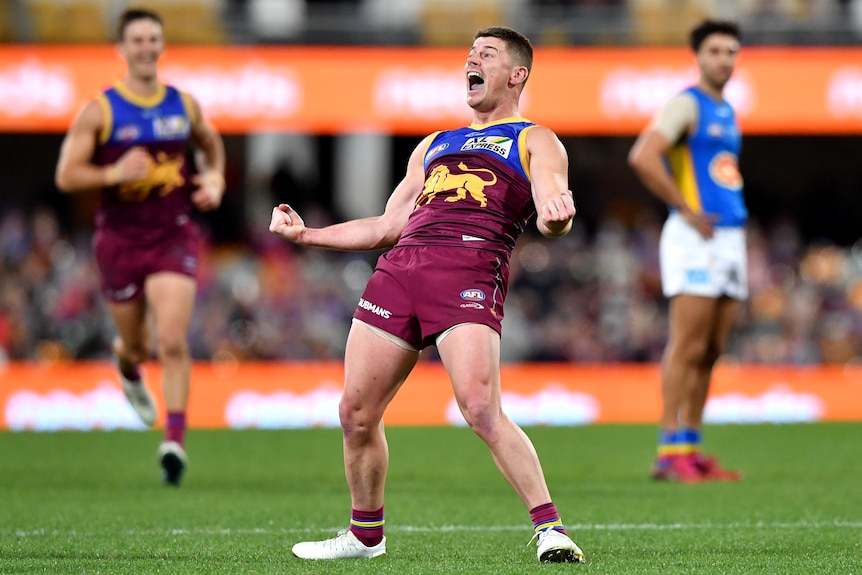 An AFL player in a maroon jersey pumps his fists and yells in jubilation 