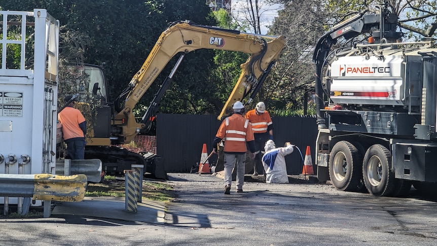 Workers in high-vis cloths work in a hole in the street.