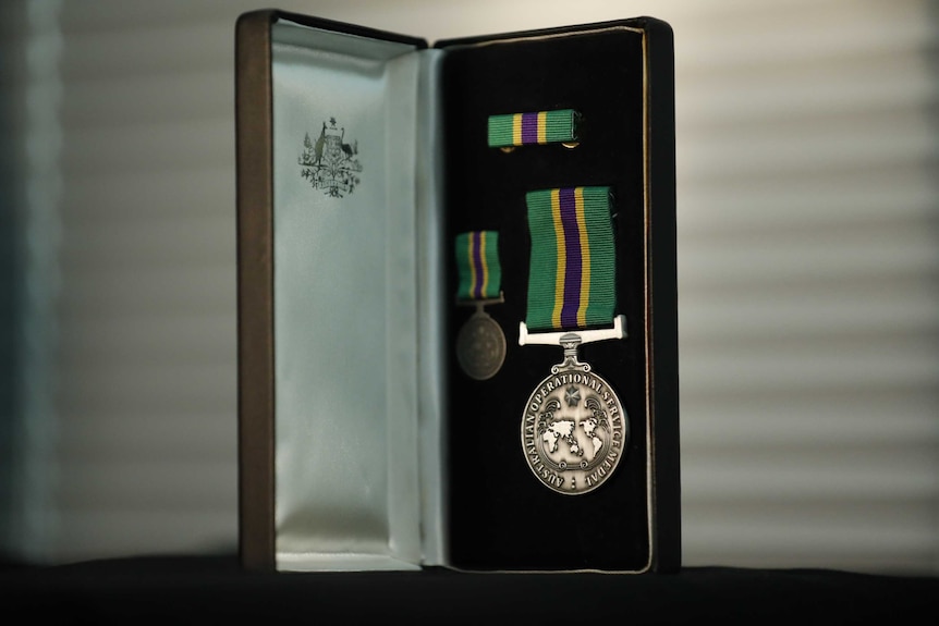 A silver Operational Service Medal with green, purple and yellow ribbon sits in a black box