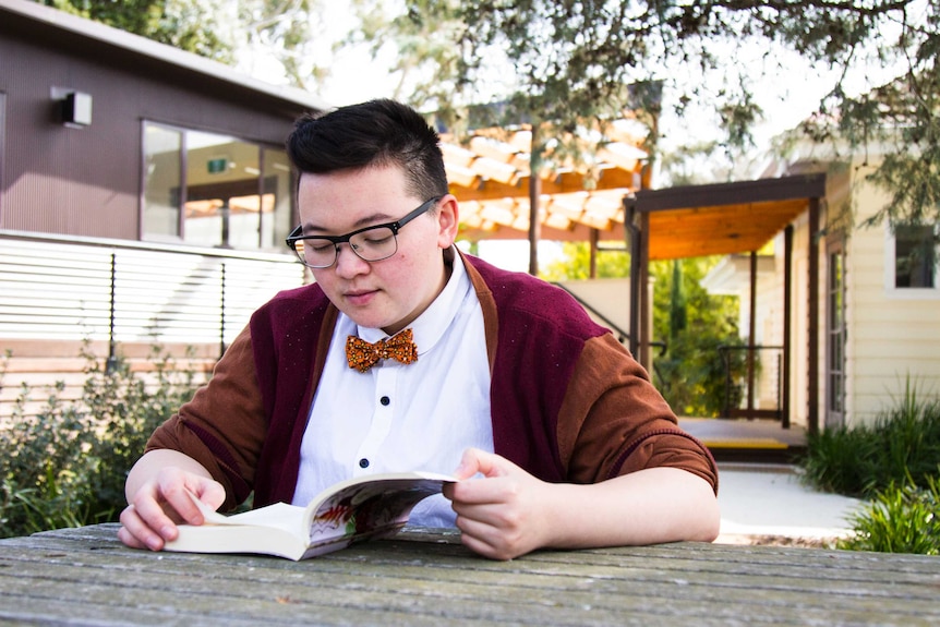 Colour photograph of person reading a book at a table outdoors.