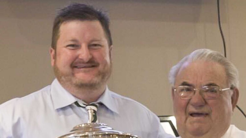 Picture of a younger man holding a silver trophy with an older man