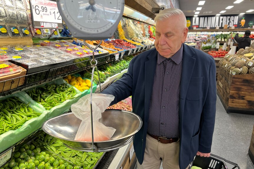 An elderly man weighs some vegetables in a green grocer store.