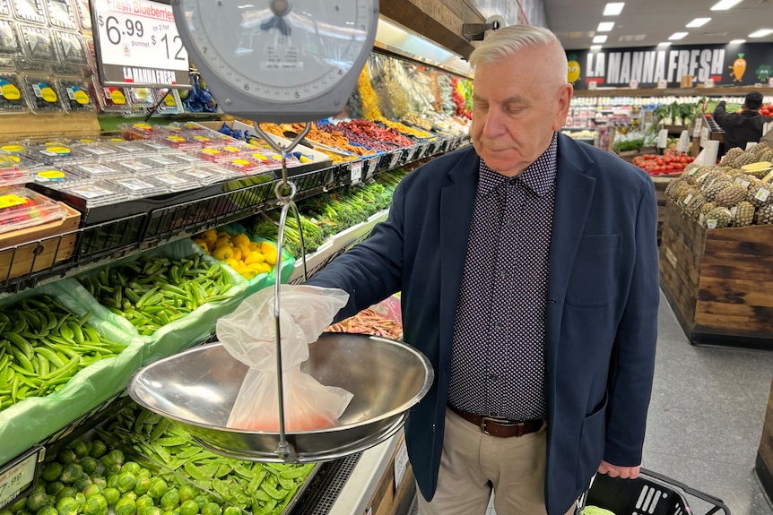 An elderly man weighs some vegetables in a green grocer store.
