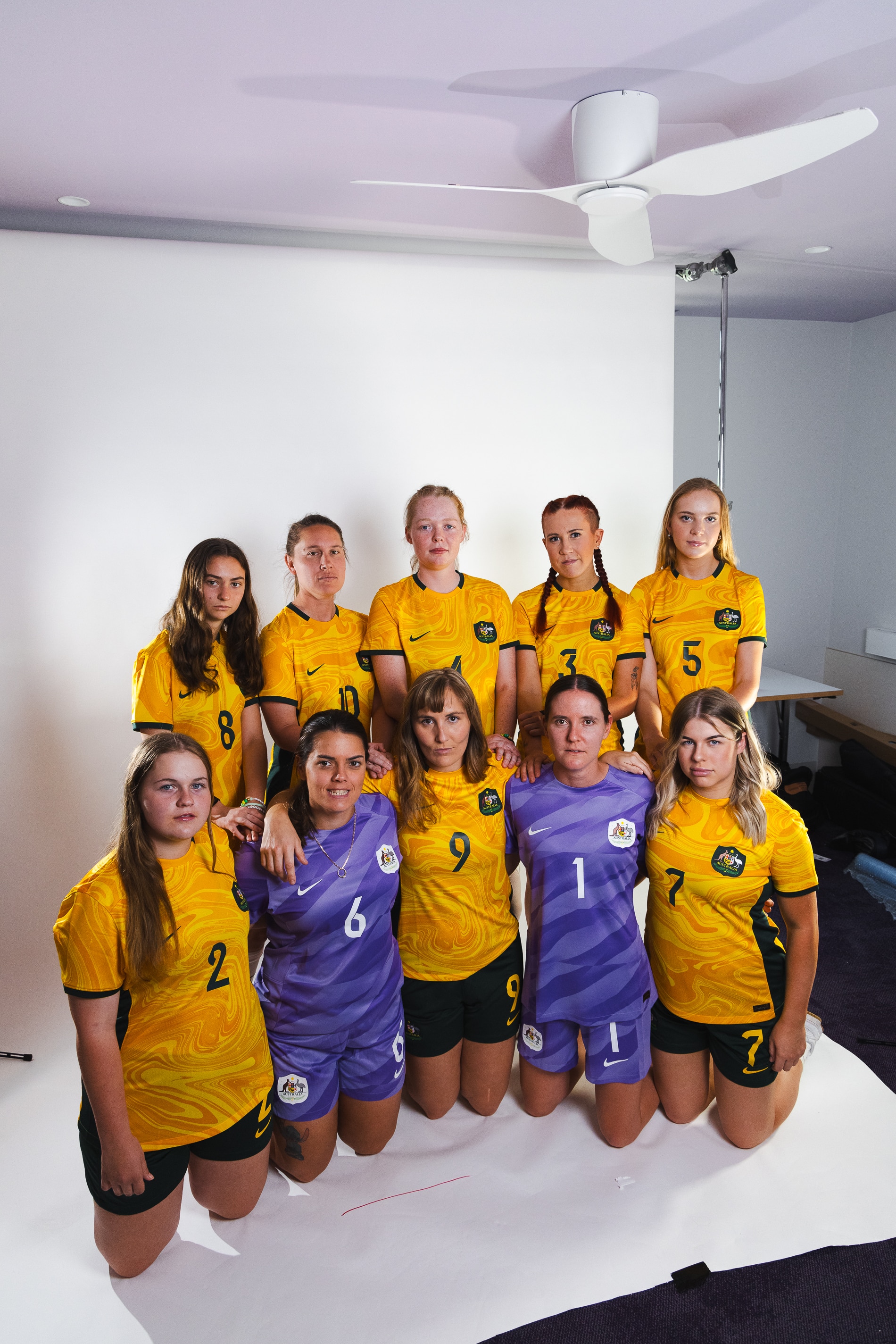 10 women, eight in green and gold soccer uniforms and two in purple goalkeeping uniforms pose for a team photo on white backdrop