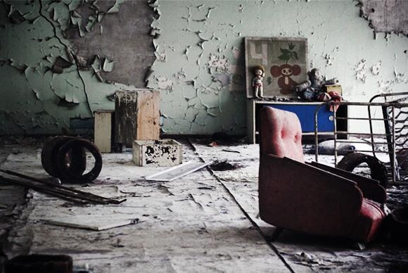 A crumbling nursery room at a primary school in Pripyat, Ukraine. There is sofa, cracked wallpaper and toys on a small cabinet.