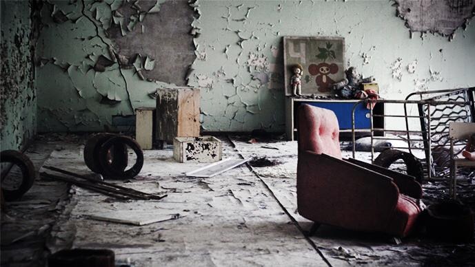 A crumbling nursery room at a primary school in Pripyat, Ukraine. There is sofa, cracked wallpaper and toys on a small cabinet.