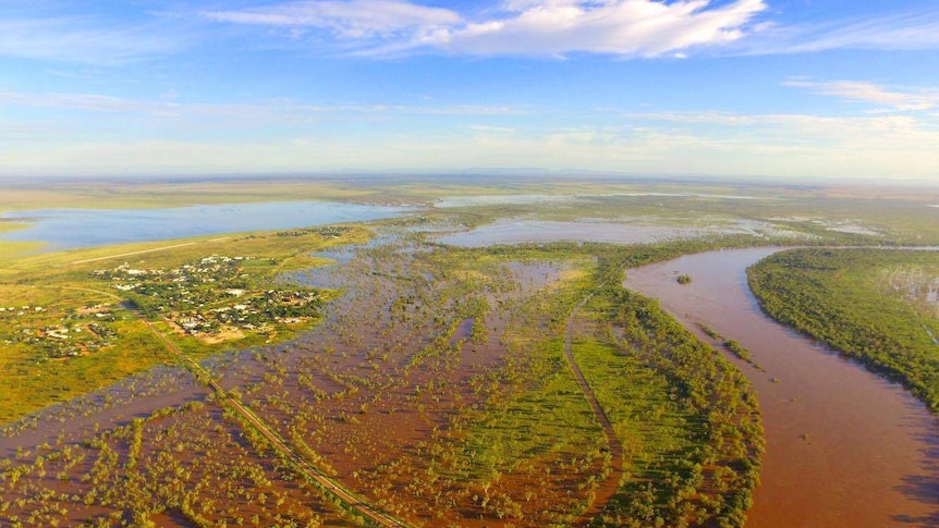 An aerial photo of the Fitzroy River in flood, edging close to houses in Fitzroy Crossing.