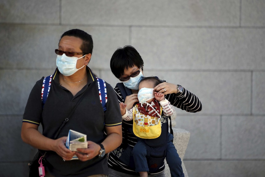 A Chinese tourist puts a mask on her child's face to prevent contracting MERS