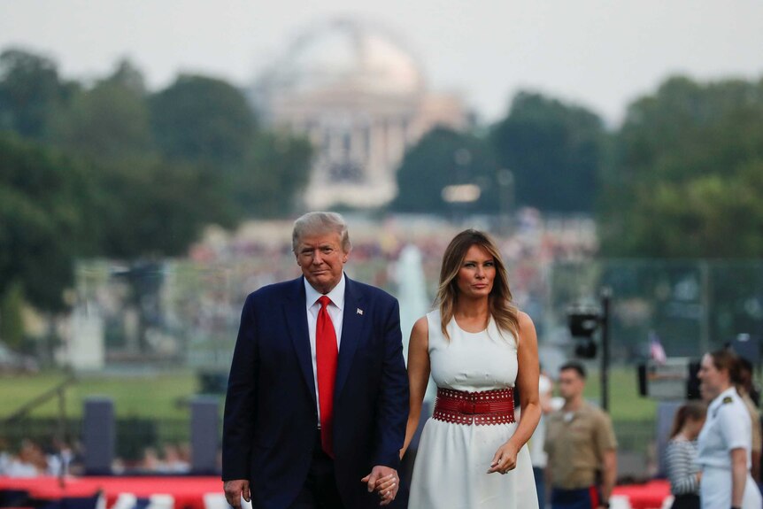 Donald Trump and Melania Trump hold hands as they walk towards the camera with the background out of focus