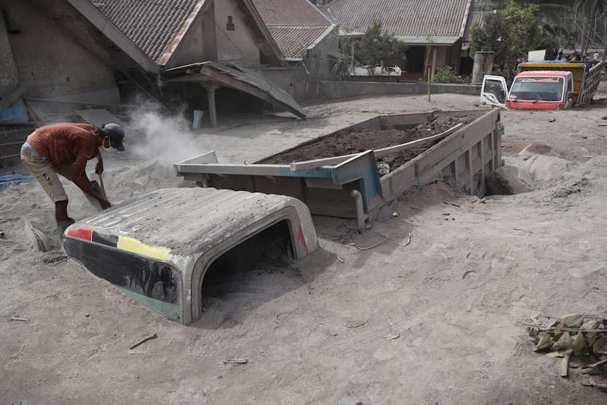 A man inspects a truck buried in the ash following the eruption of a volcano