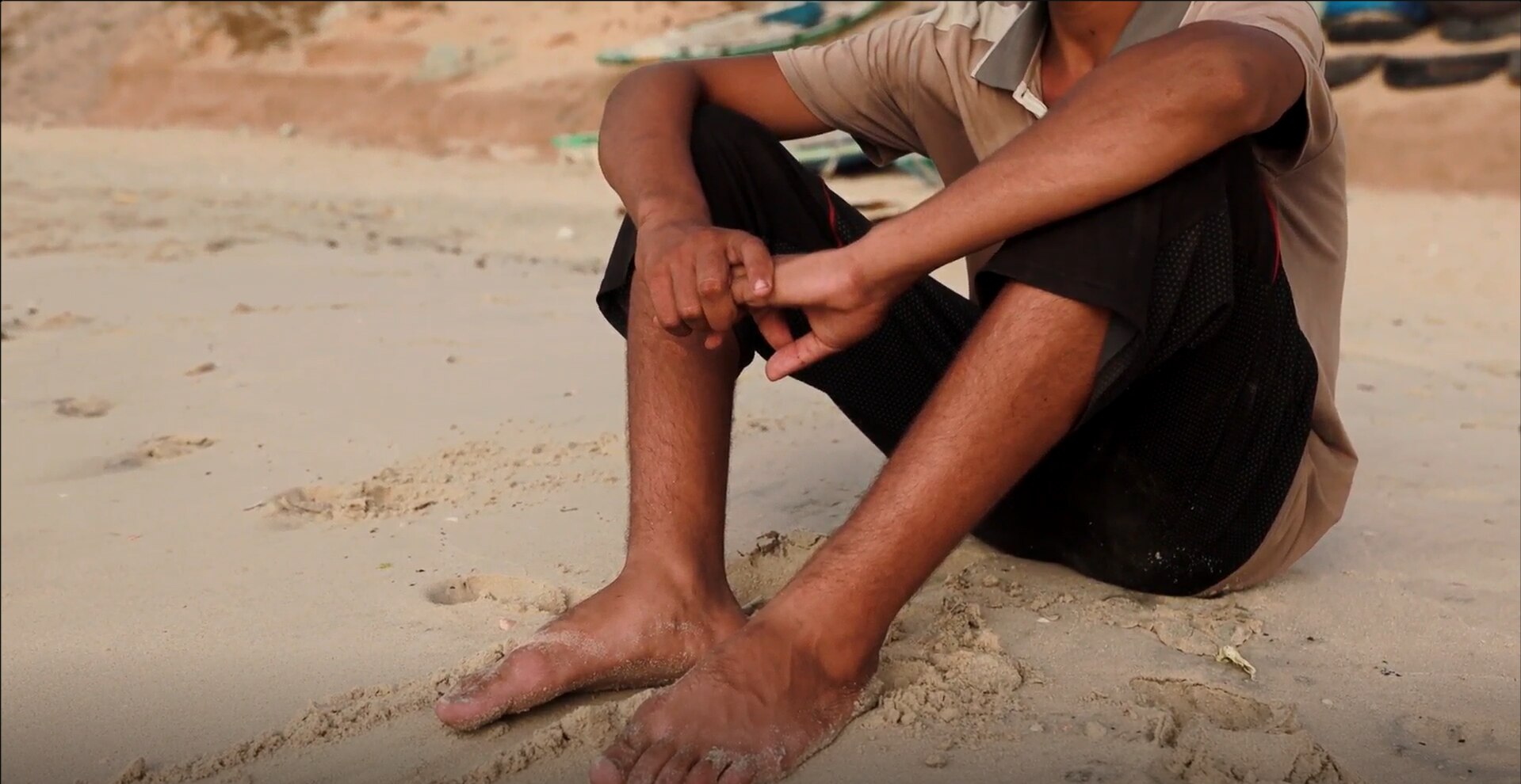 A boy with his arms on his knees sitting on a beach