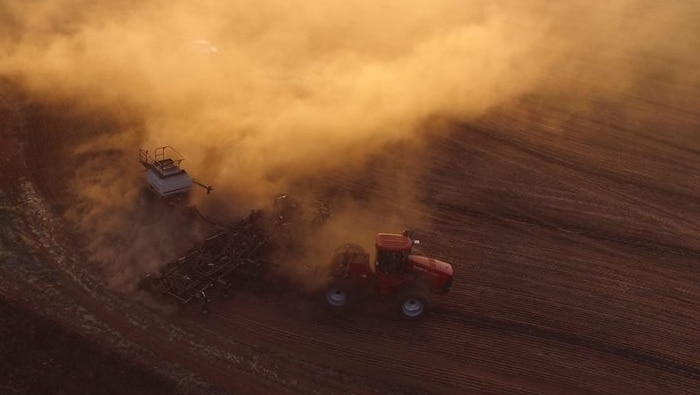 an aerial shot of a tractor pulling a crop seeder through dusty paddock. it's clear from the thick dust that the soil is dry.