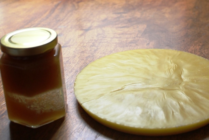 A jar of honey and a circular piece of wax on a dining room table