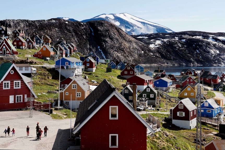 People walk through a neighbourhood in Greenland overlooking an icy mountain vista