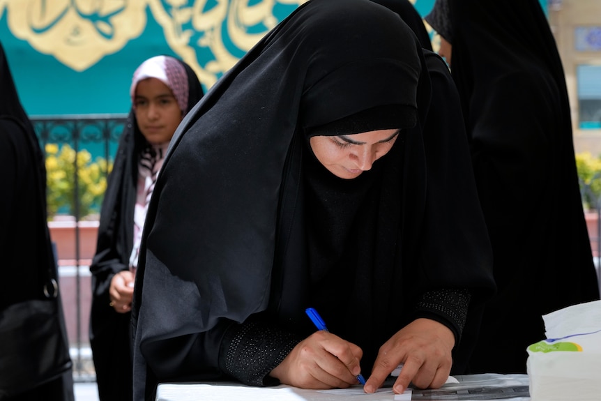 A young woman in a black chador fills out a voting ballot.