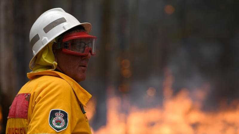 A firefighter in helmet and goggles against a burning backdrop.