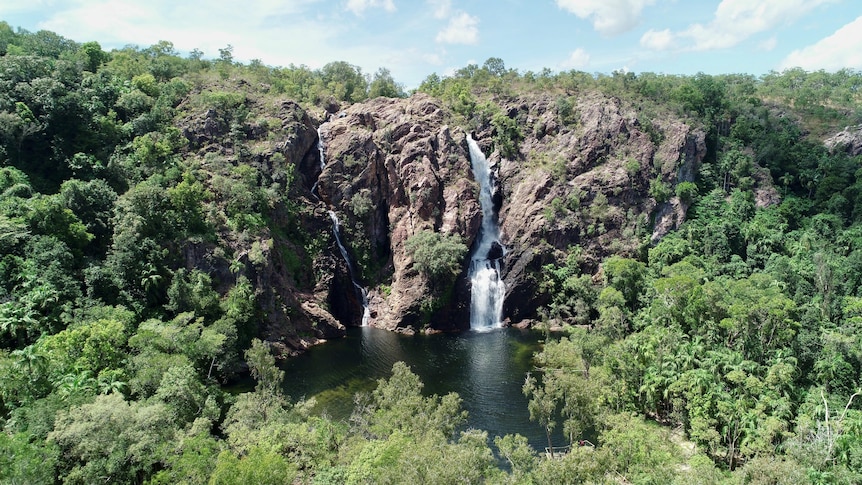 A high-up view of a waterfall on a rocky ridge, with a blue pool below.