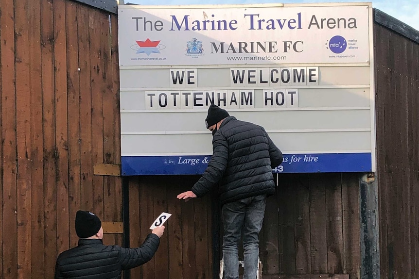 Man standing on letters puts up 'welcome' sign outside stadium.