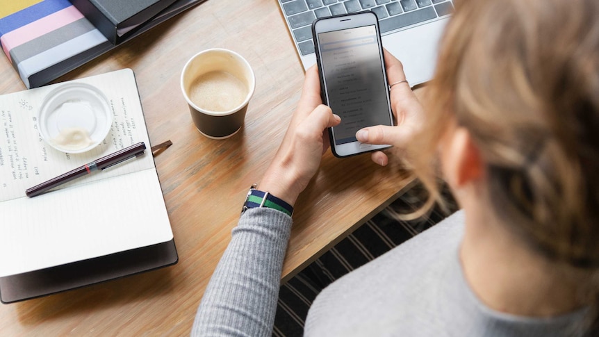 A woman looks at a smartphone while working, depicting someone using social media at work.