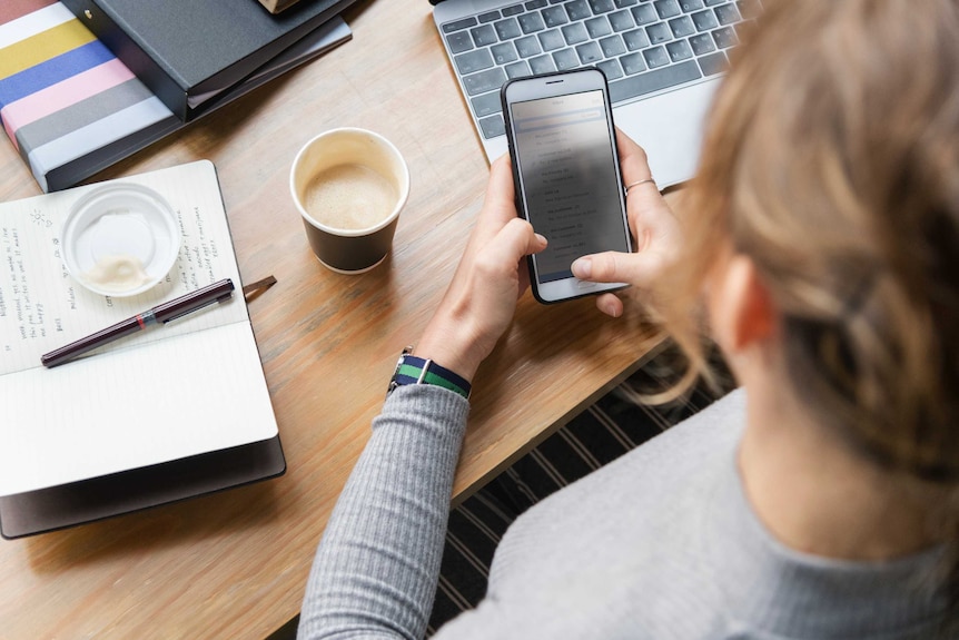 A woman looks at a smartphone while working, depicting someone using social media at work.