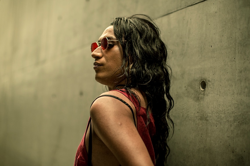 Colour photo of artist Akashi Fisiinaua standing in front of concrete wall.