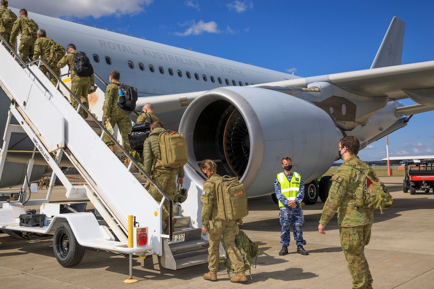 A number of troops wearing camouflage uniforms board a plane on a sunny day