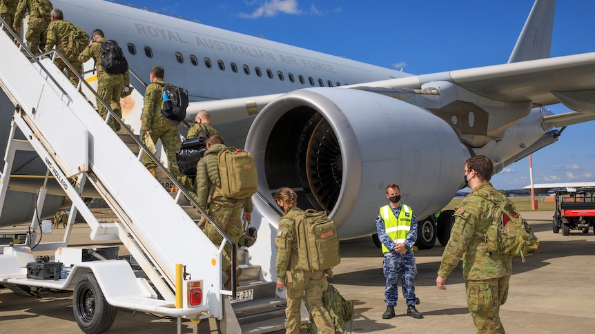 A number of troops wearing camouflage uniforms board a plane on a sunny day