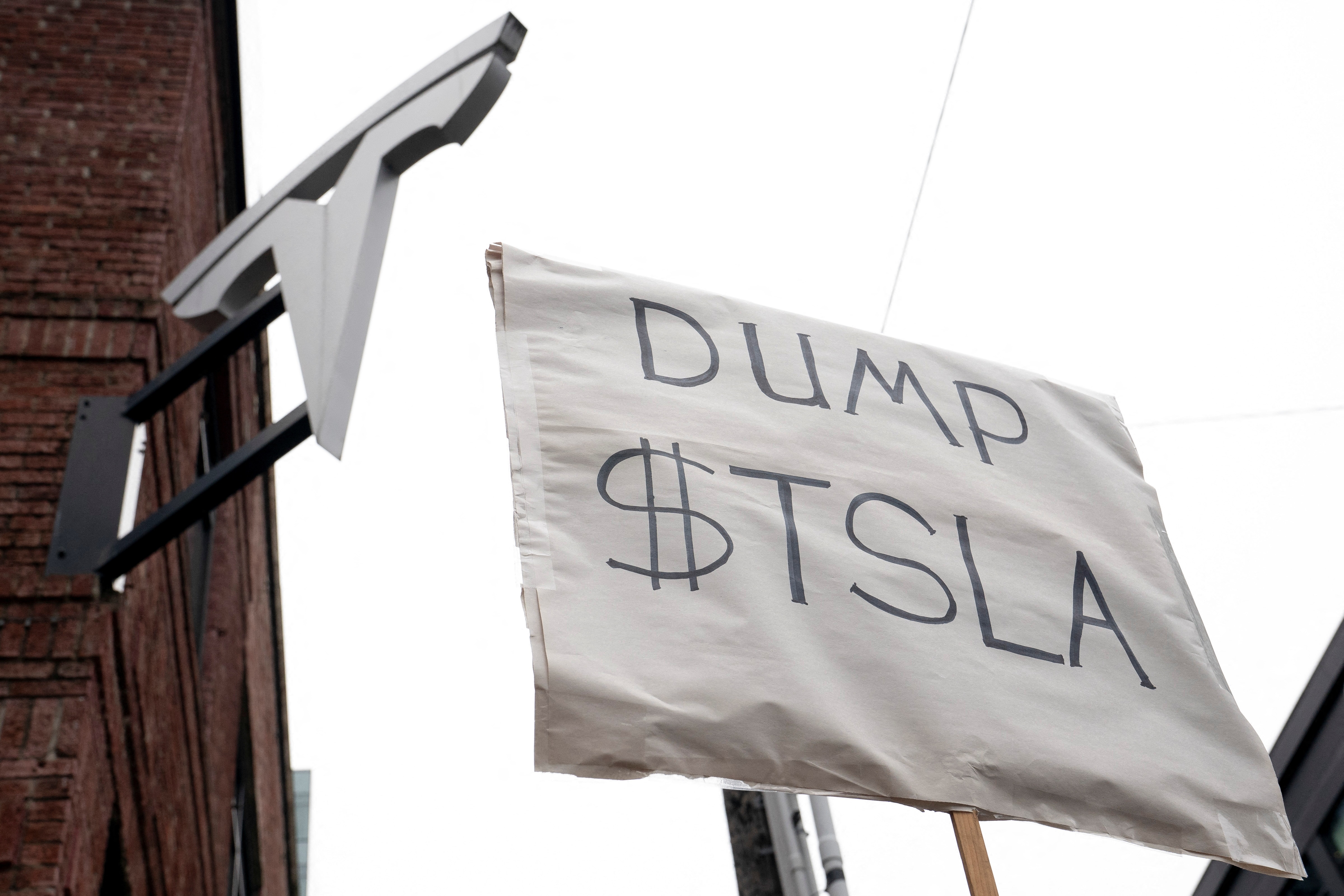 A sign telling people to dump Tesla shares held in front of a Tesla showroom.
